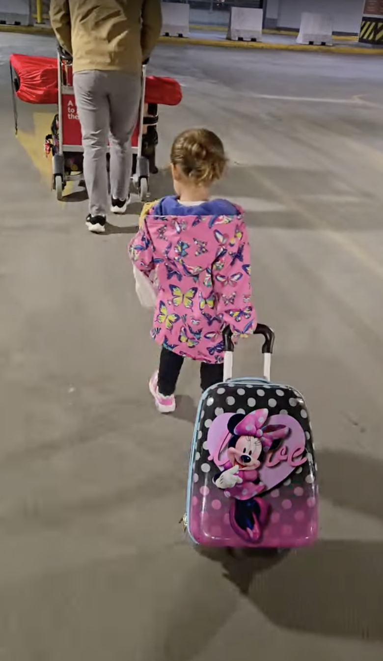 Young child pulling a Minnie Mouse suitcase while travelling with family during a Disney vacation