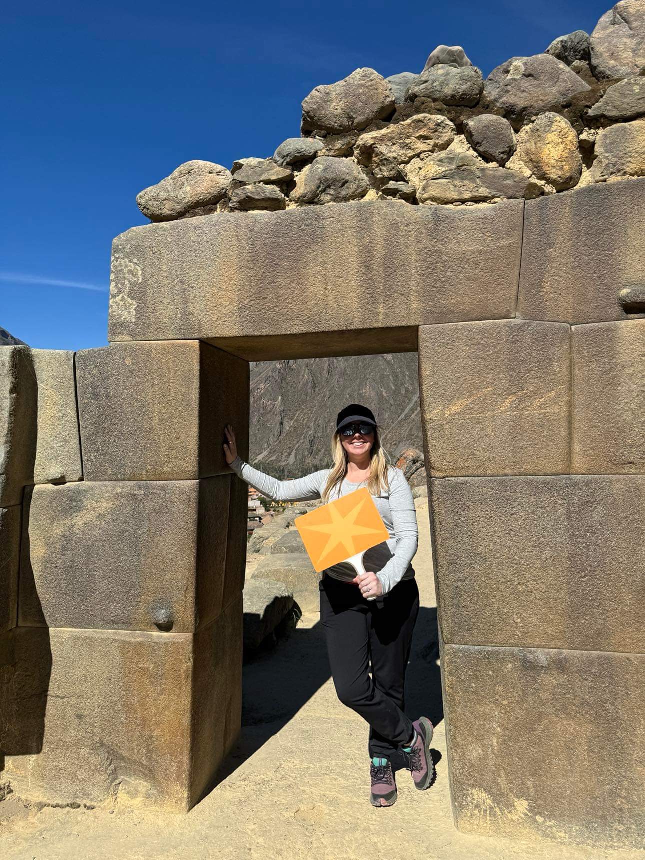 TriciTraveller holding an Adventures by Disney flag while standing in a stone doorway at a historic site in Peru.