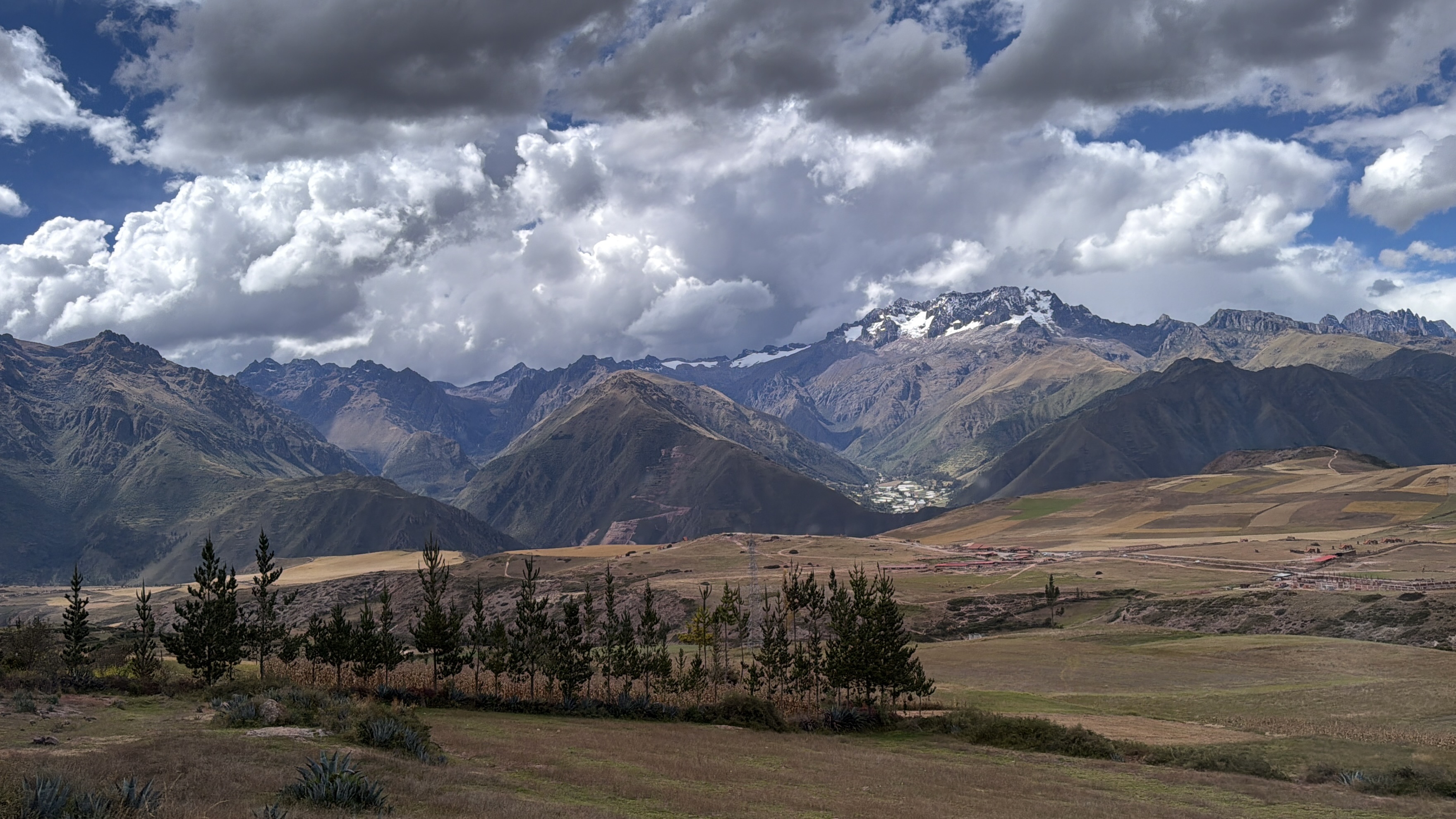 Wide view of the Andes mountains in Peru beneath large clouds, with fields and a valley below.